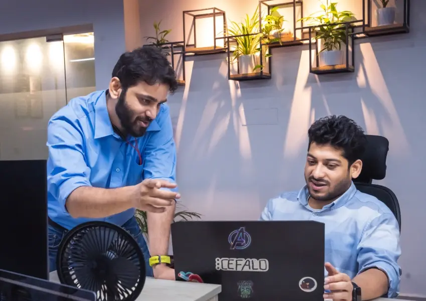 Two-developers-discussing-project-work-at-a-desk-with-laptops-and-a-plant-wall-in-the-background