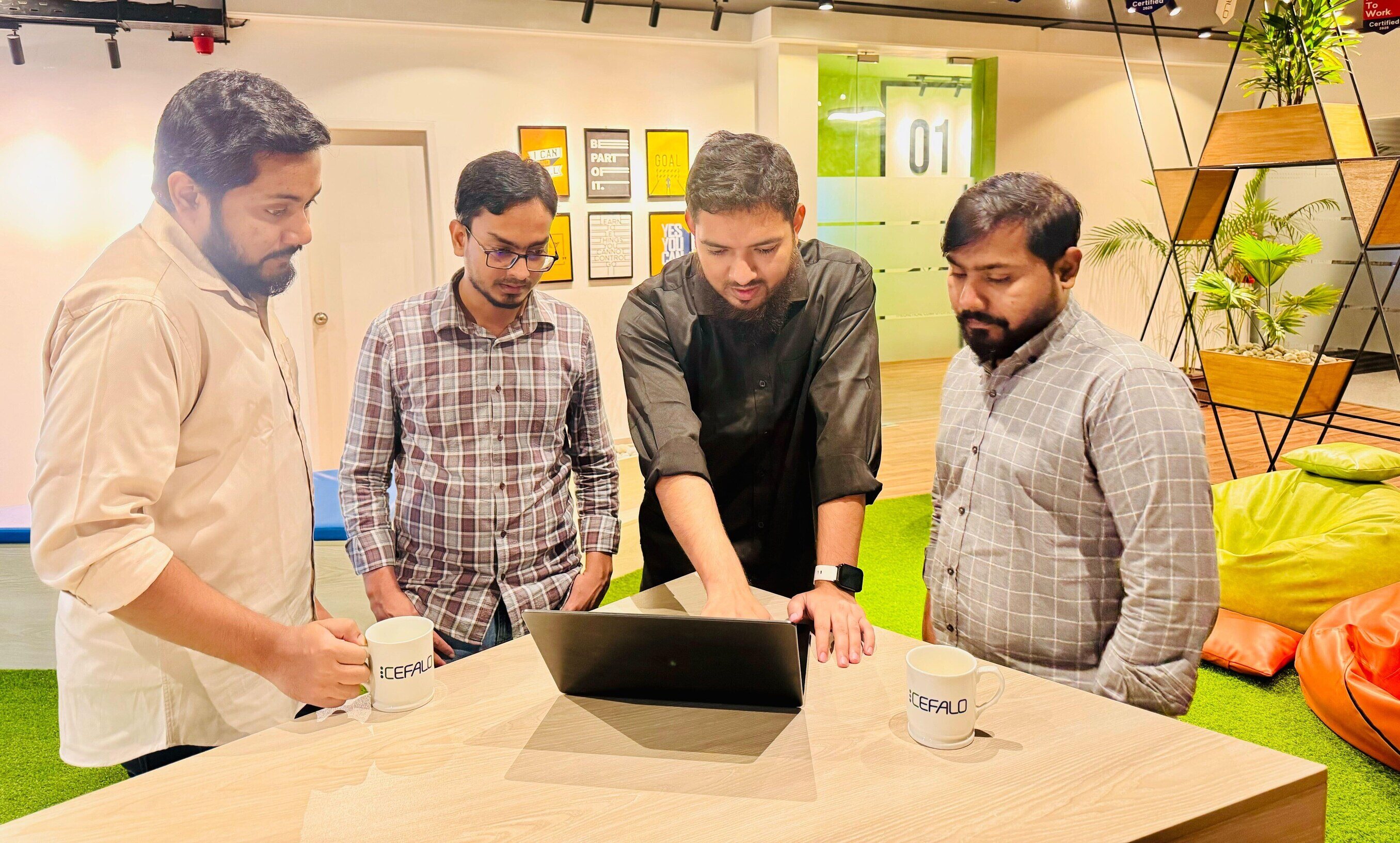 Four men around a table with a computer on it, discussing something work related